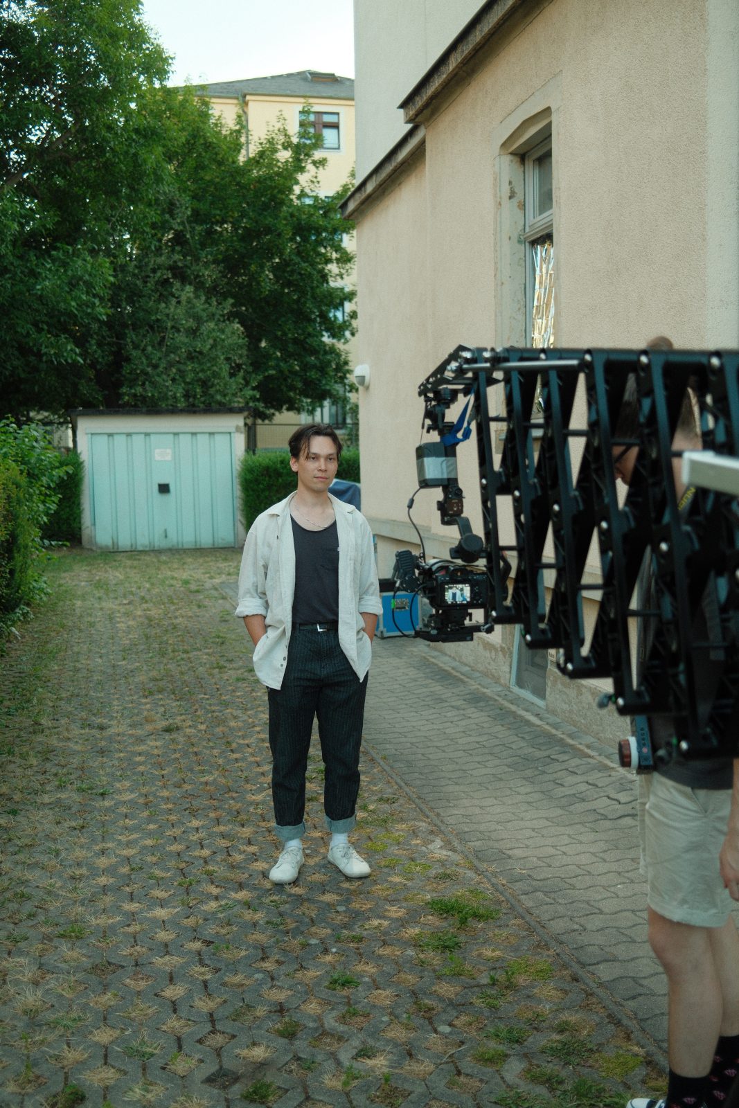 Darsteller auf einem gepflasterten Hof, rechts daneben Kamerarig und Team