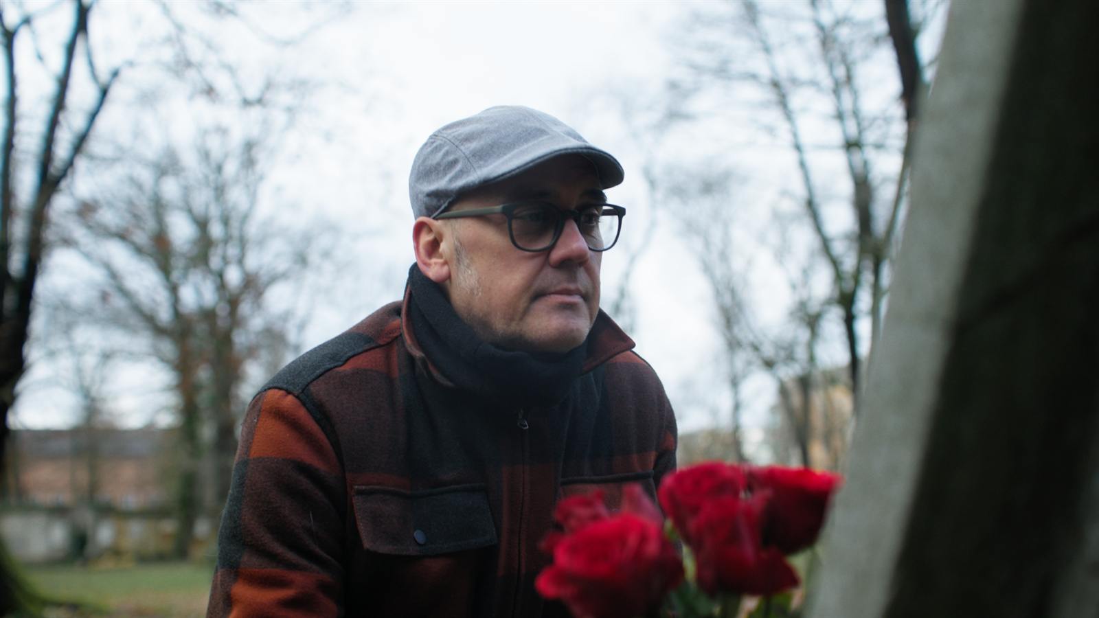 Mann mit Schiebermütze und Brille hält einen Strauß roter Rosen