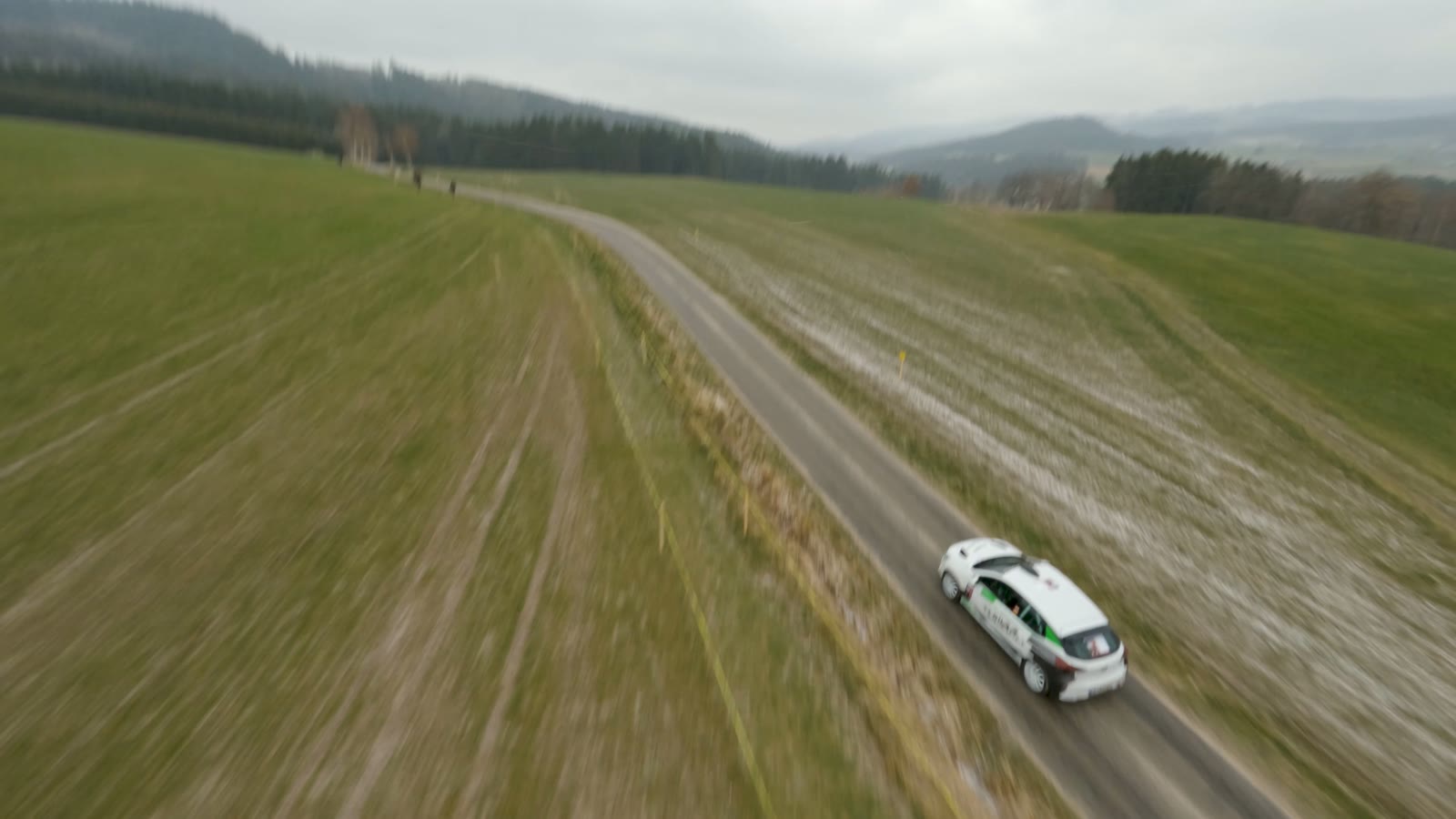 Luftaufnahme: der Rallyewagen auf einem Feldweg zwischen Wiesen